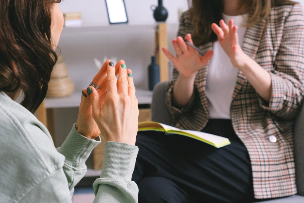 Close-up of a therapy session, with the client speaking and gesturing with hands, while the therapist listens attentively, taking notes