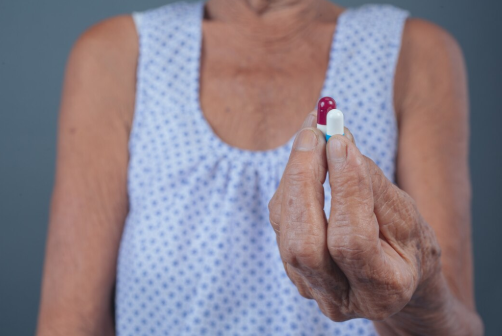 A senior woman examining a large pill held between her fingers