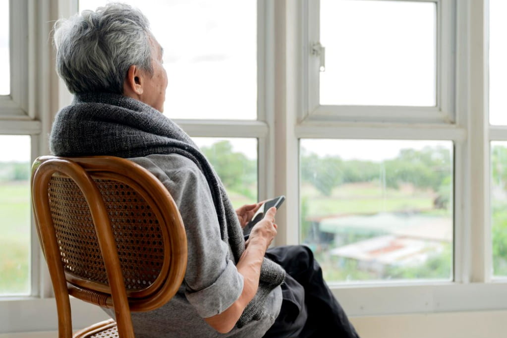 An elder sitting by the window, holding a phone in his hands