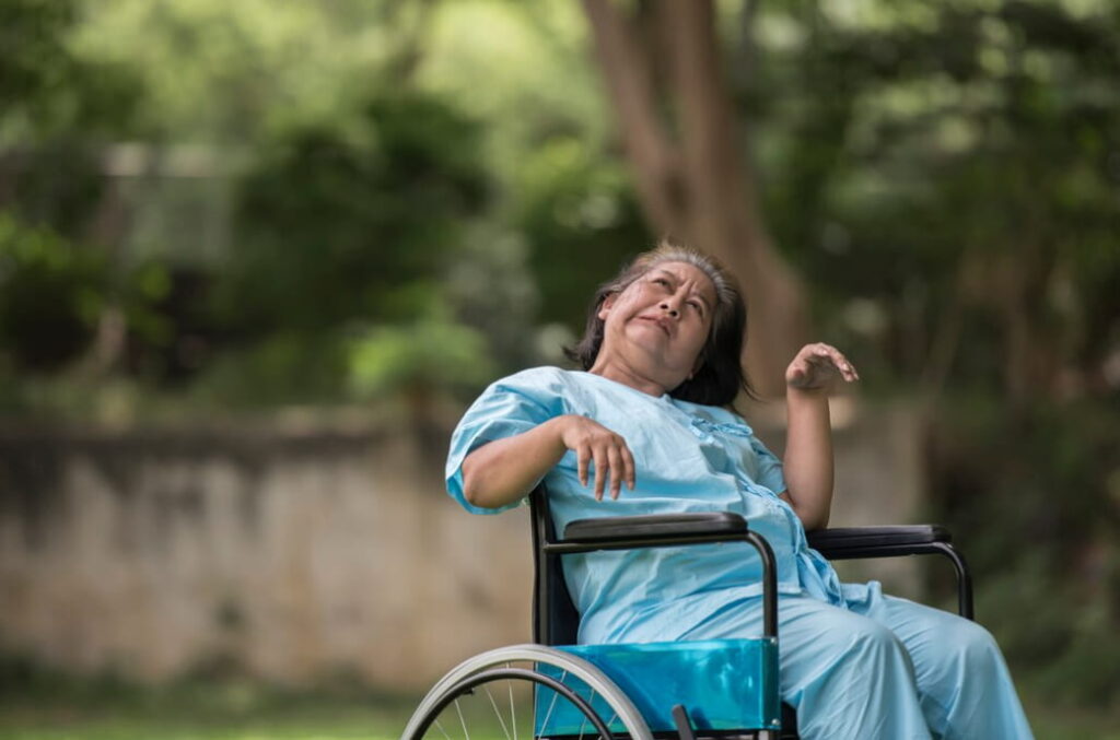 An elderly woman in a wheelchair appears contemplative in a garden